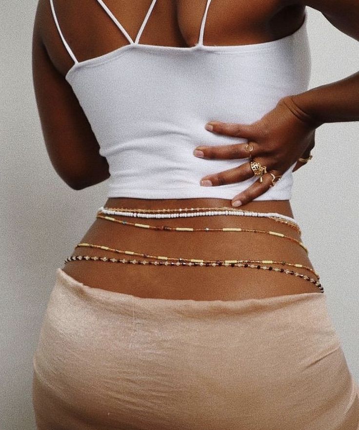 girl with a white tank top wearing unique handmade waist beads made in Ghana. She is wearing 5 waist beads of different colour. White waist beads, Gold waist beads and Blue and gold waist beads.